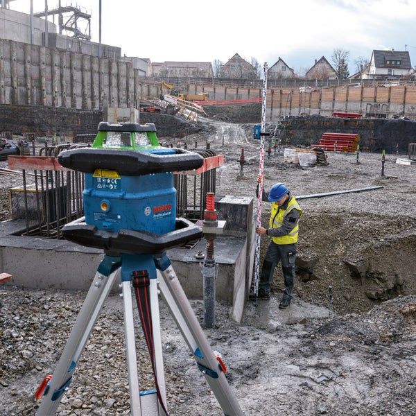 Baustelle mit Rotationslaser auf Stativ und Bauarbeiter mit Messlatte