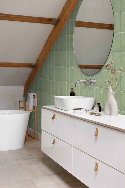 Modernes Badezimmer mit grünen Wandfliesen, weißem Waschtisch, Aufsatzwaschbecken, runder Wandspiegel und freistehender Badewanne unter Dachschräge.