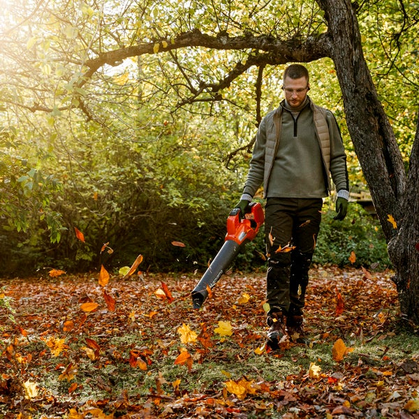 Mann benutzt einen Laubbläser im Garten, um Herbstlaub zu entfernen.