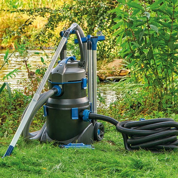 Teichsauger mit Zubehör und Schläuchen auf einer Wiese an einem Teich.