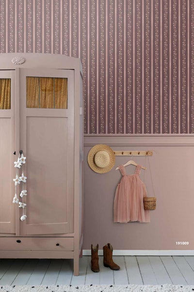 Wandgestaltung mit floral gestreifter Tapete, Wandfarbe, Holzschrank und dekorativem Zubehör wie Strohhut und Kinderkleid.