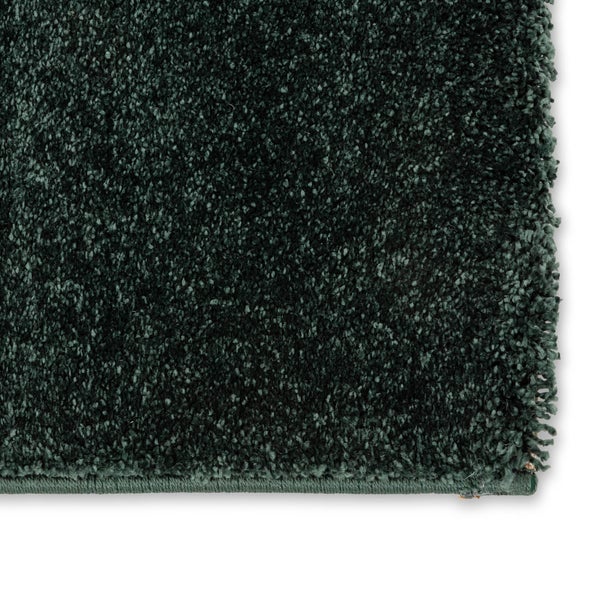 Dunkelgrüner Hochflor-Teppich mit weicher Oberfläche und geketteltem Rand.