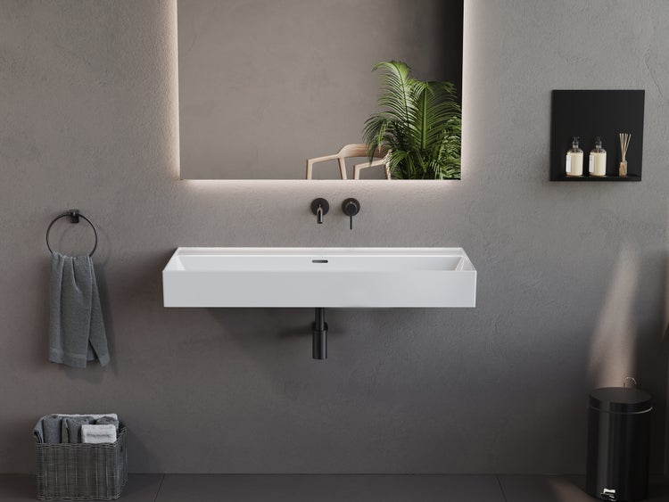 Modernes Badezimmer mit weißem Wand-Waschtisch, hinterleuchtetem Spiegel, schwarzen Armaturen und Accessoires vor einer grauen Wand.