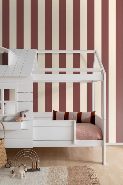 Gestreifte Tapete mit vertikalen Bahnen in Dunkelrot und Creme hinter einem weißen Kinderhausbett aus Holz in einem hellen Kinderzimmer.