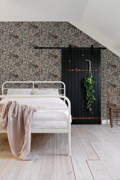 Schlafzimmer mit weißem Bett, Holzboden, Schiebetür und Tapete mit Waldmotiven.