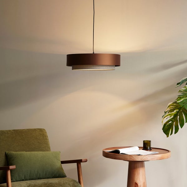 Moderne Pendelleuchte über einem runden Holztisch und einem grünen Sessel in einem hellen, wohnlichen Zimmer.