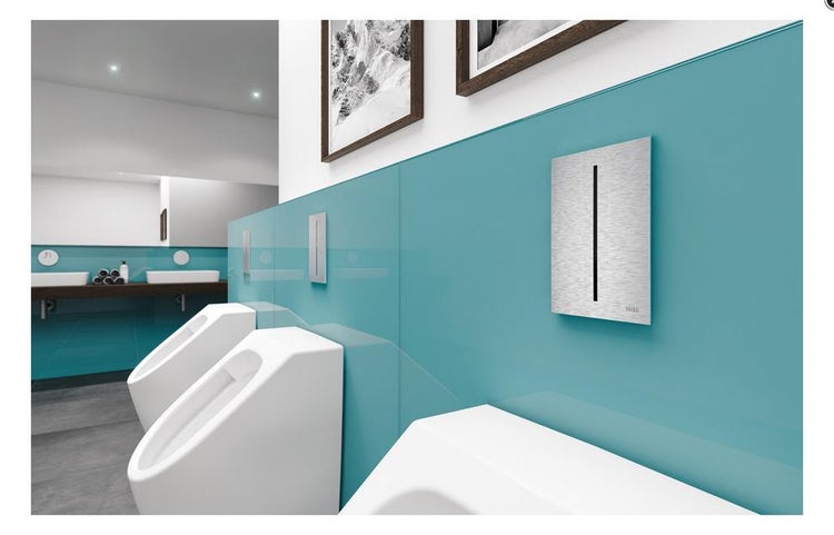 Moderne Sanitäreinrichtung mit weißen Urinalen, türkisfarbener Glaswand und Betätigungsplatten aus gebürstetem Edelstahl.