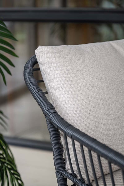 Detail eines grauen Gartenstuhls mit Polyrattan-Geflecht und beigem strukturiertem Sitzkissen aus Stoff für den Außenbereich.