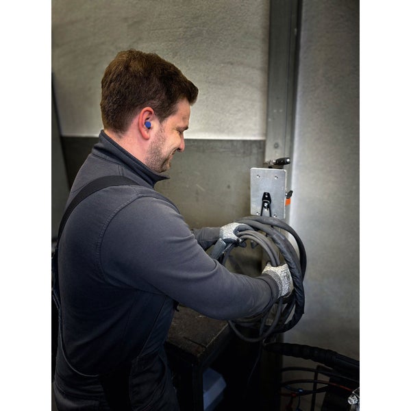 Ein Mann arbeitet mit einem Winkelschleifer an einem Metallstück in einer Werkstatt, beleuchtet von einer Arbeitsleuchte.