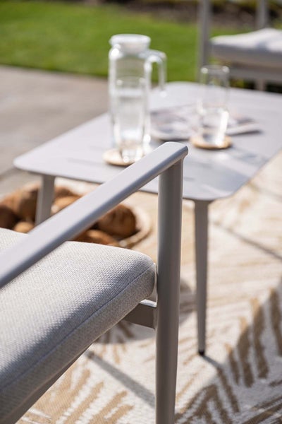 Moderner Gartenstuhl mit Polster und Beistelltisch in hellem Außenbereich auf einem gemusterten Außenteppich.