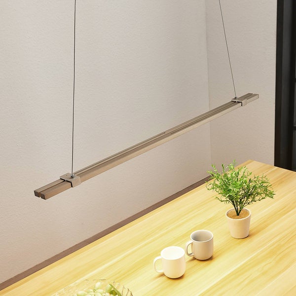 Moderne, lineare LED-Pendelleuchte aus Metall über einem hellen Esstisch aus Holz mit Tassen und einer Zimmerpflanze.