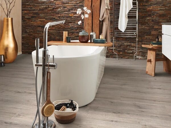 Modernes Badezimmer mit freistehender Badewanne, Armatur, Holzablage und Wandverkleidung aus Natursteinoptik auf einem Holzboden.
