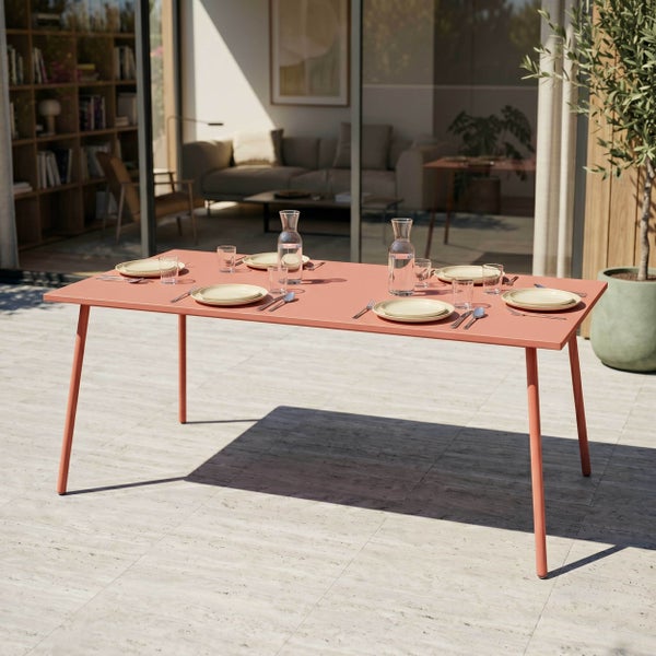 Rechteckiger Gartentisch aus Metall auf einer hellen Terrasse, eingedeckt für sechs Personen vor einem modernen Wohnbereich mit Glasfront.