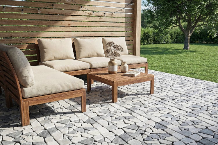 Holz Lounge Gruppe auf einer Terrasse mit Natursteinpflaster vor einer Holzlamellenwand im Garten.