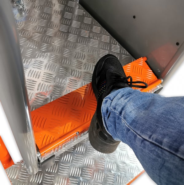 Fuß in schwarzem Sneaker und blauer Jeans auf einer orangefarbenen rutschhemmenden breiten Stufe einer Aluminiumleiter.