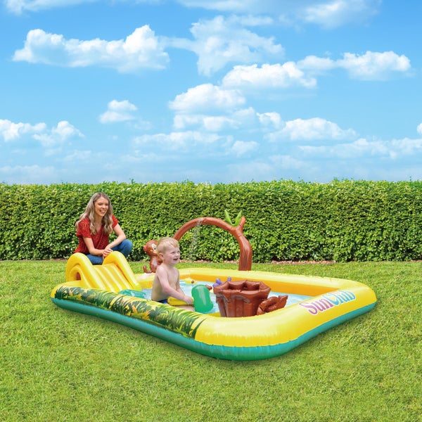 Kind spielt im aufblasbaren SunClub Spielecenter mit Rutsche und Wassersprühfunktion im Garten, während eine Frau daneben kniet.