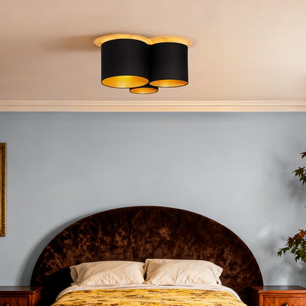 Dreiflammige Deckenleuchte mit schwarzen Stoffschirmen und goldener Innenseite, montiert in einem Schlafzimmer über dem Bett.