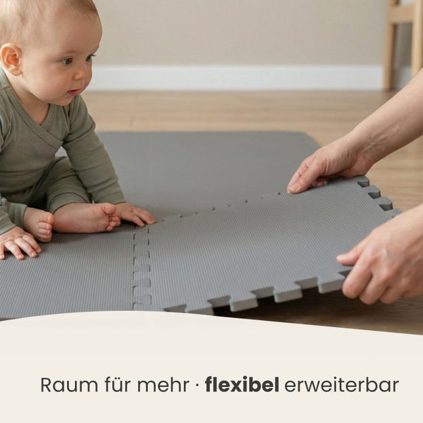 Baby sitzt auf grauer Schaumstoff-Puzzlematte, während ein Erwachsener ein weiteres Teil anfügt, flexibel erweiterbar.