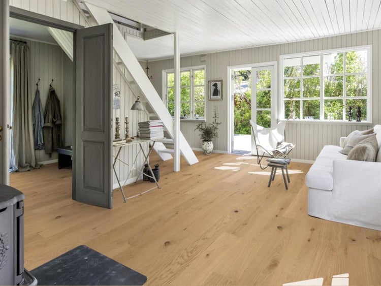 Heller Raum mit Parkettboden aus Eiche, weißen Holzwänden, Treppe, Sofa und großen Fenstern.