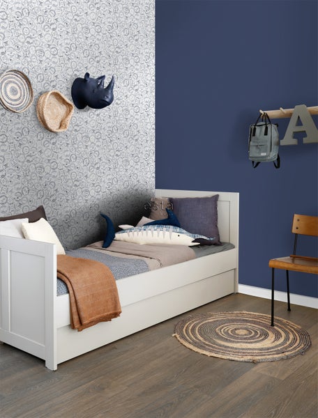 Kinderzimmer mit weißem Bett, gemusterter Tapete und dekorativen Accessoires.