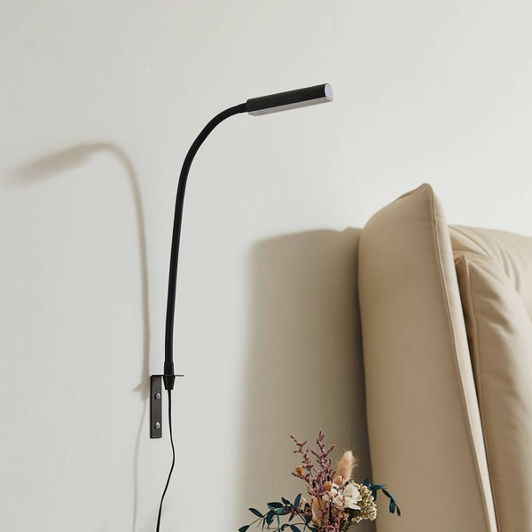 Schwarze flexible Wand-Leseleuchte mit Schwanenhals, montiert an einer Wand neben einem gepolsterten Kopfteil.