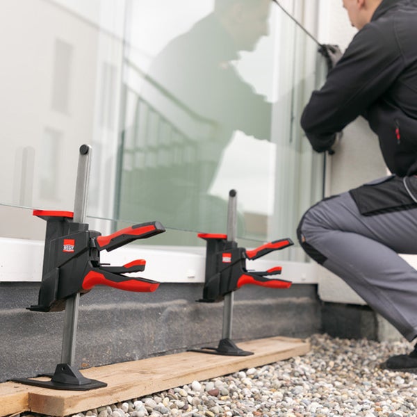 Ein Handwerker montiert eine Glasscheibe unter Verwendung von Bessey Einhandzwingen zur Fixierung auf einer Baustelle.
