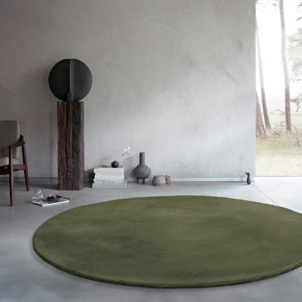 Runder moosgrüner Teppich in einem minimalistischen Wohnraum mit Sichtbetonwänden und moderner Dekoration.