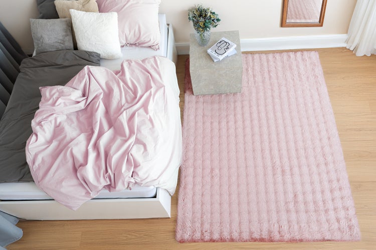 Ein rechteckiger Hochflorteppich mit Struktur liegt neben einem Bett in einem modern eingerichteten Schlafzimmer mit Parkettboden.