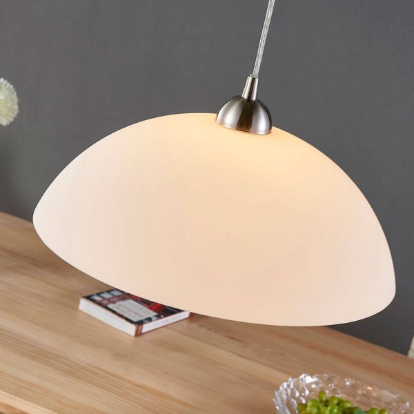 Pendelleuchte mit kuppelförmigem weißem Glasschirm und gebürsteter Metallfassung über einem Holztisch.