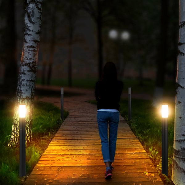 Szene mit Wegbeleuchtung und einer Person auf einem Holzpfad im Garten bei Nacht.