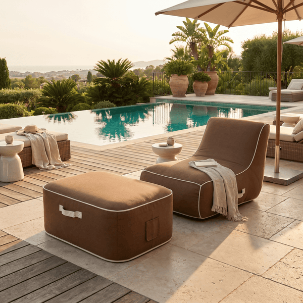Heller Lounge-Bereich im Freien mit einem braunen Stoff-Sitzsack und passendem Hocker auf einer Holzterrasse neben einem Pool.