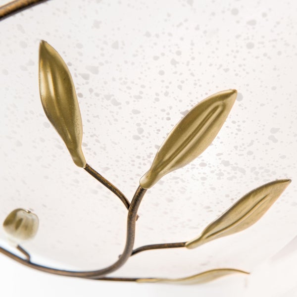 Detailansicht einer Lampe mit Glaslampenschirm und dekorativem Metallzweig mit Blättern