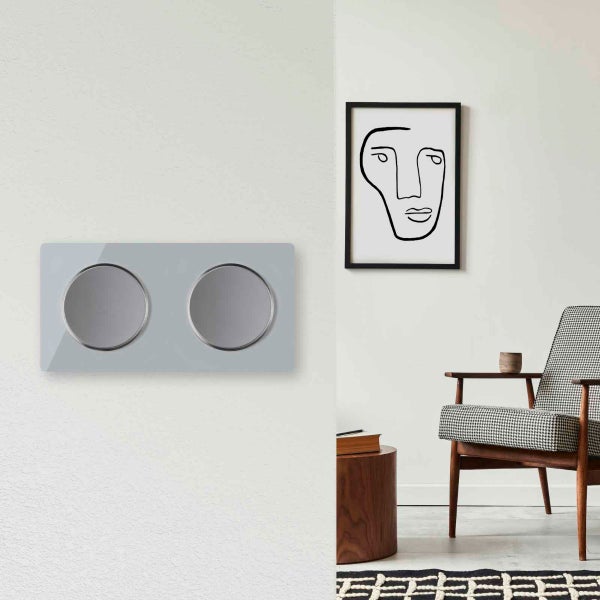 Doppellichtschalter mit runden Wippen in einem modernen Wohnraum mit Sessel und Wandbild.