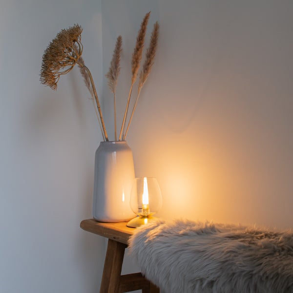 Dekorative Szene mit Lampe, Vase und Trockenblumen auf einem Hocker