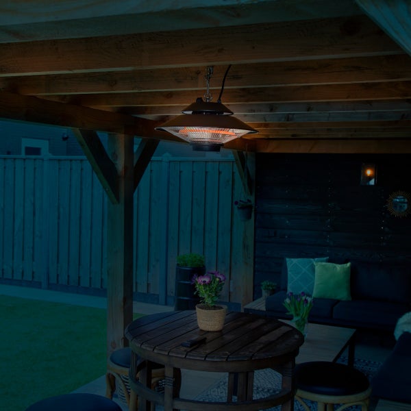 Hängender Infrarot-Terrassenheizstrahler montiert an einer Holzpergola über einem runden Holztisch im Außenbereich.