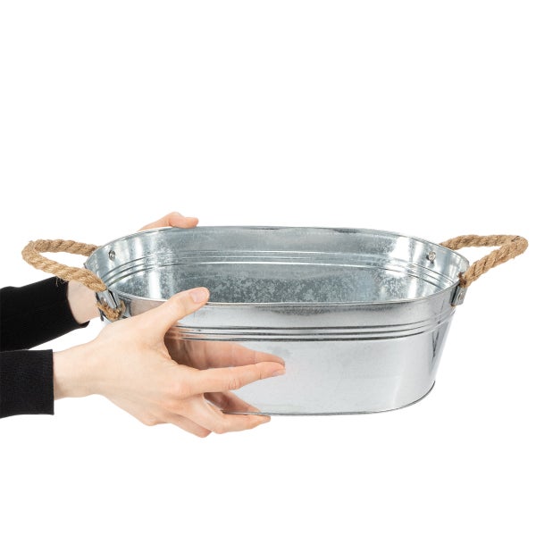 Hände halten eine ovale Zinkwanne mit Seilgriffen.