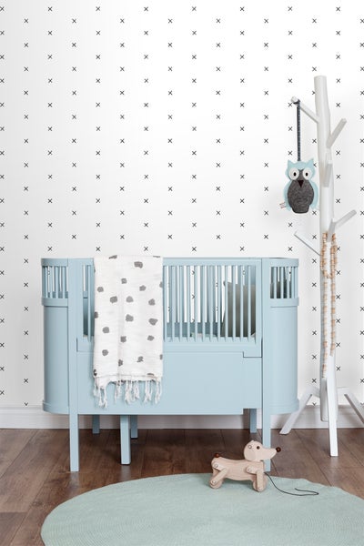 Ein Kinderzimmer mit einem blauen Kinderbett, einem weißen Kleiderständer in Baumform und einem hellblauen runden Teppich.