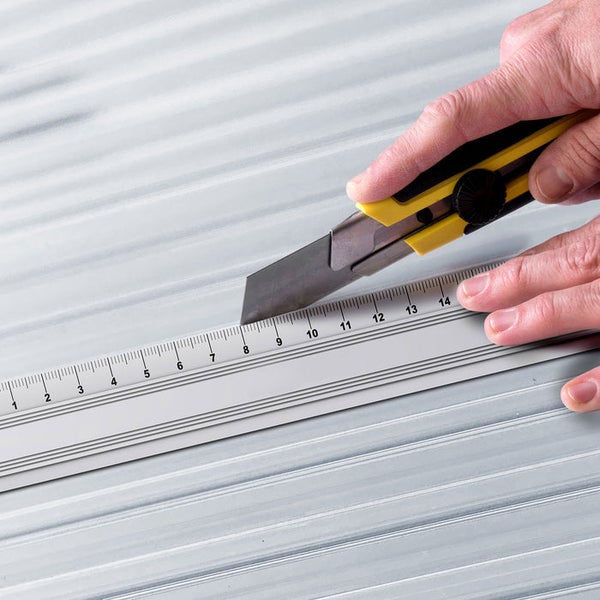 Eine Person schneidet mit einem Teppichmesser entlang eines Lineals.