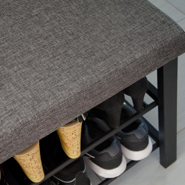 Gepolsterte Schuhbank mit grauem Stoffbezug und schwarzem Metallrahmen zur Aufbewahrung von Schuhen.