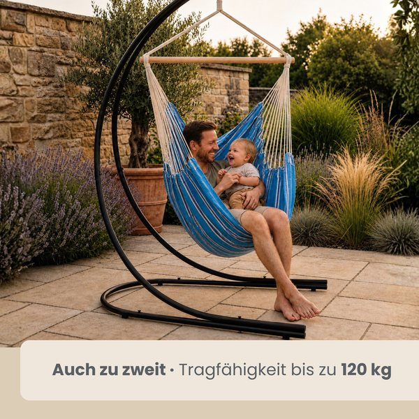 Vater und Kind sitzen gemeinsam in einem Hängesessel mit Gestell auf einer Steinterrasse im Garten.