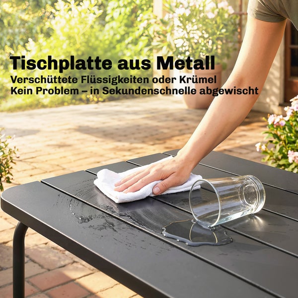 Eine Hand wischt mit einem Tuch verschüttete Flüssigkeit von einer dunklen Metalltischplatte eines Gartentisches ab.