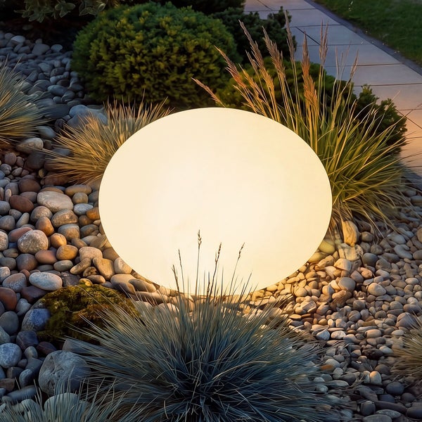 Leuchtende Gartenkugel in einem Steingarten mit Ziergräsern und Gehweg.