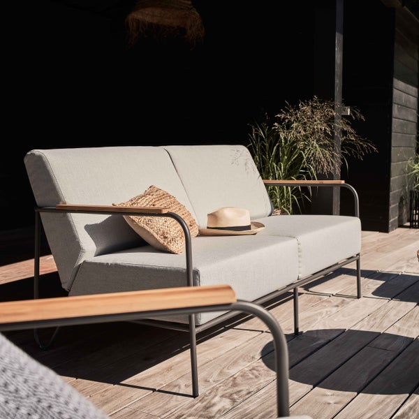 Modernes 2-Sitzer Gartensofa mit hellgrauen Polstern, dunkelgrauem Metallgestell und Holzarmlehnen auf einer Holzterrasse.
