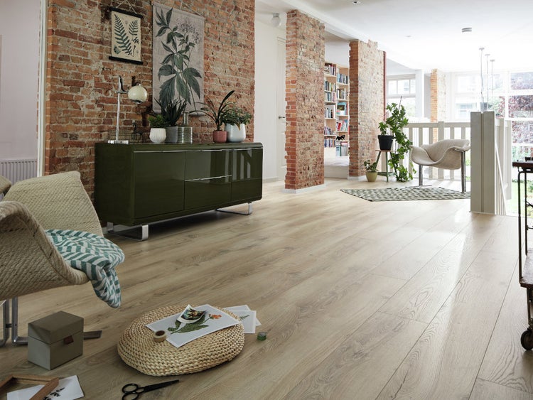 Geräumiger Wohnraum mit Laminatboden in Holzoptik, Sichtmauerwerk, modernem Sideboard und stilvollen Sitzmöbeln in einem lichtdurchfluteten Interieur