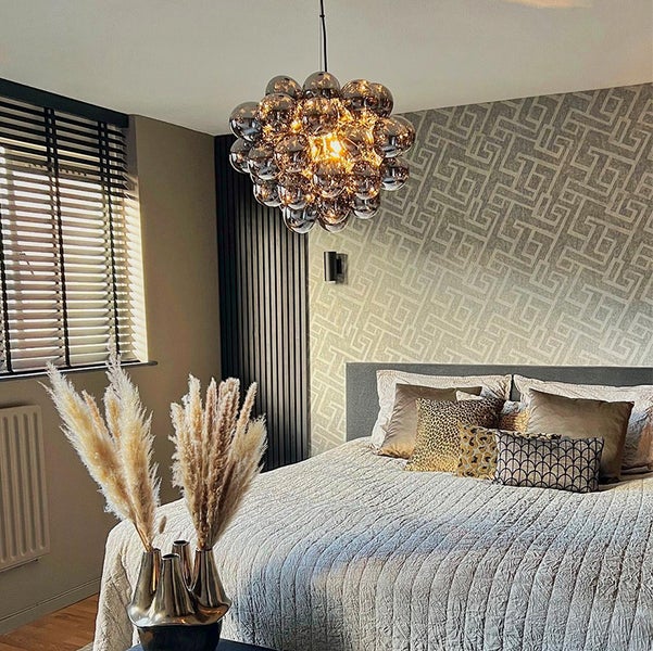 Schlafzimmer mit Bett, dekorativen Kissen, Vase mit Ziergras und kugelförmiger Pendelleuchte