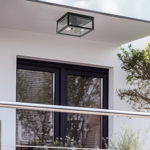 Quadratische Außen-Deckenleuchte aus schwarzem Metall und Glas, montiert an einem weißen Dachvorsprung über einem dunklen Fensterrahmen.
