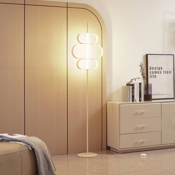 Moderne Stehleuchte mit drei geschwungenen Schirmen in einem hellen Wohnzimmer neben einer Kommode und einer Holzwand.
