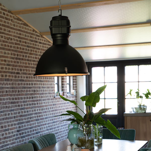 Schwarze Hängelampe über Esstisch in einem Raum mit Backsteinmauer