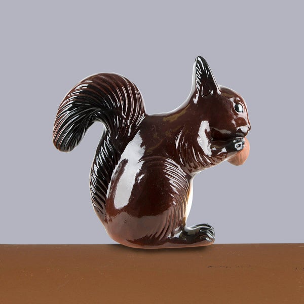 Braune, glänzend glasierte Eichhörnchen-Figur aus Keramik, sitzend mit einer Eichel.