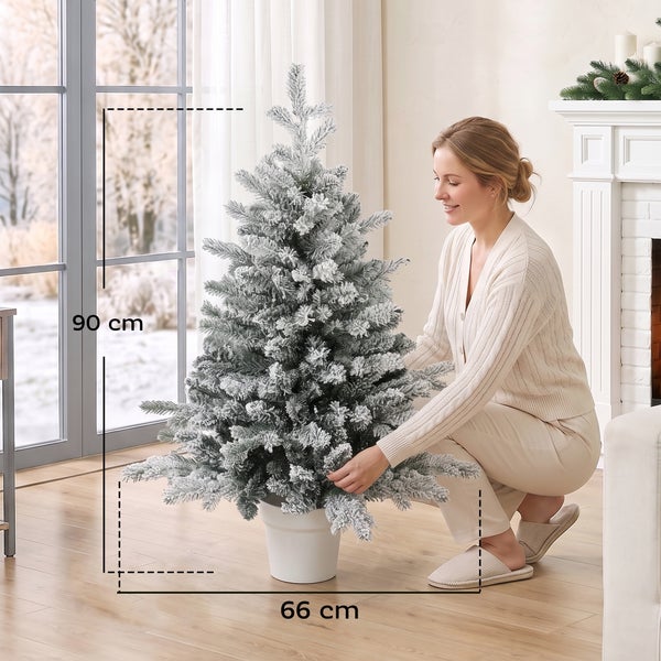 Künstlicher Weihnachtsbaum mit Schnee im Topf, 90 Zentimeter hoch und 66 Zentimeter breit, aufgestellt in einem hellen Wohnzimmer.